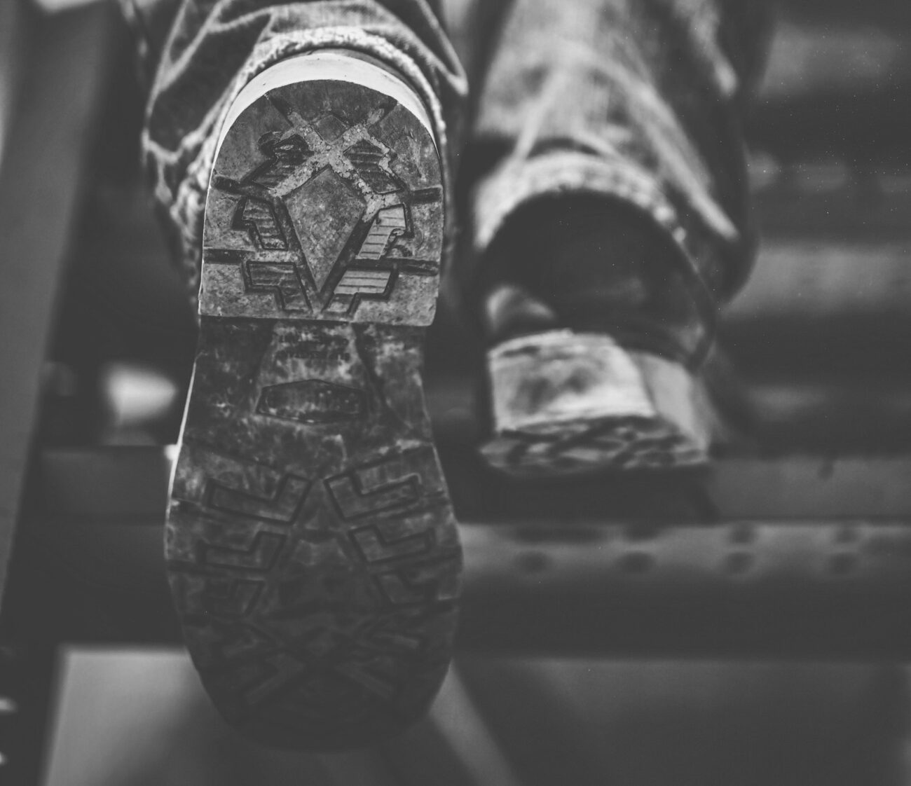 Black and white close-up of a hiking boot's sole mid-step, showing a deep lug tread from heel to toe