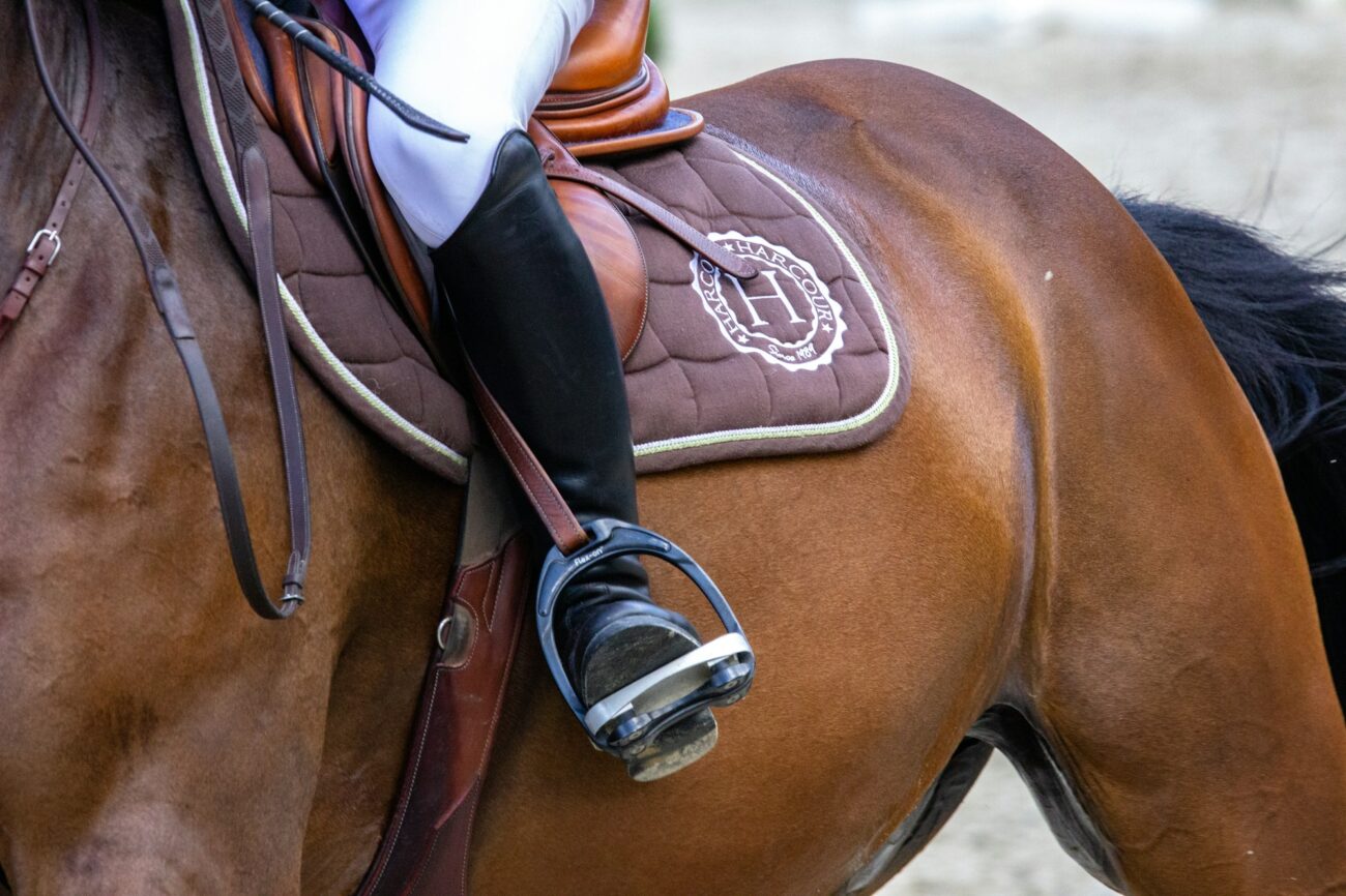 A rider's black tall boot in a stirrup on a bay horse, the boot heel sitting just behind the stirrup tread