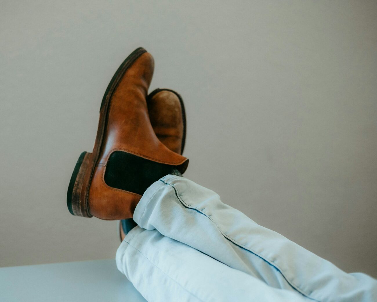 Brown leather ankle boots with elastic side panels and a low stacked heel, crossed at the ankle above light jeans